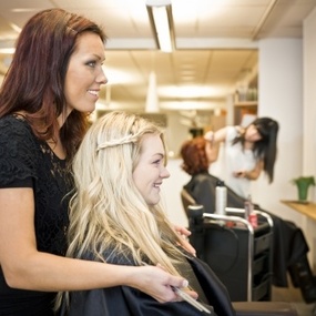 Friseurin stylt einer Kundin die Haare im modernen Friseursalon mit Spiegel und Pflanzen.